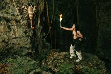 woman with torch looking at giant scorpion in cave