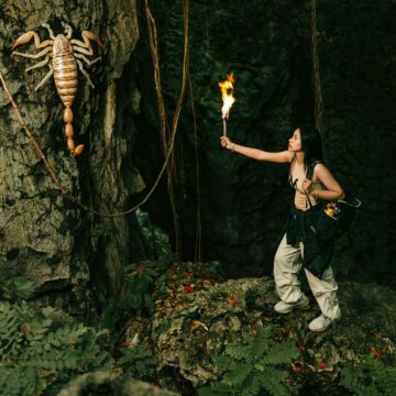 woman with torch looking at giant scorpion in cave