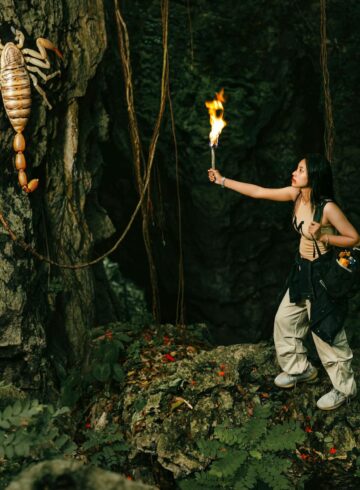 woman with torch looking at giant scorpion in cave
