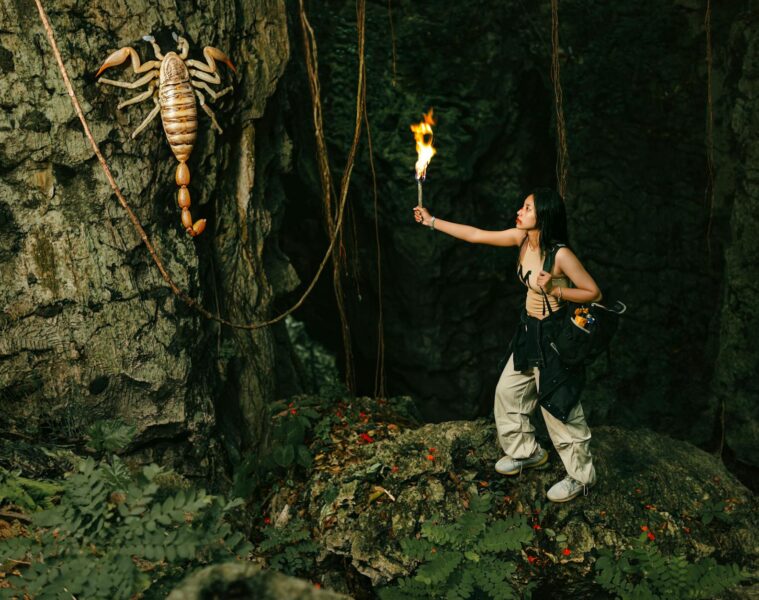 woman with torch looking at giant scorpion in cave