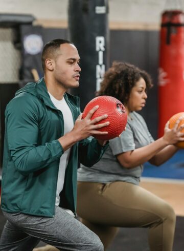strong multiracial trainer and sportswoman doing lunges with balls in gym