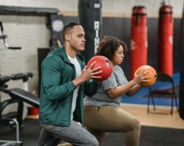 strong multiracial trainer and sportswoman doing lunges with balls in gym