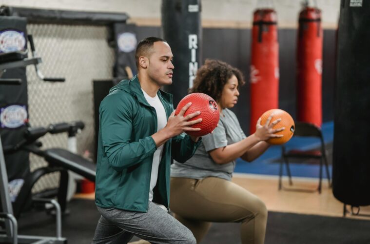 strong multiracial trainer and sportswoman doing lunges with balls in gym