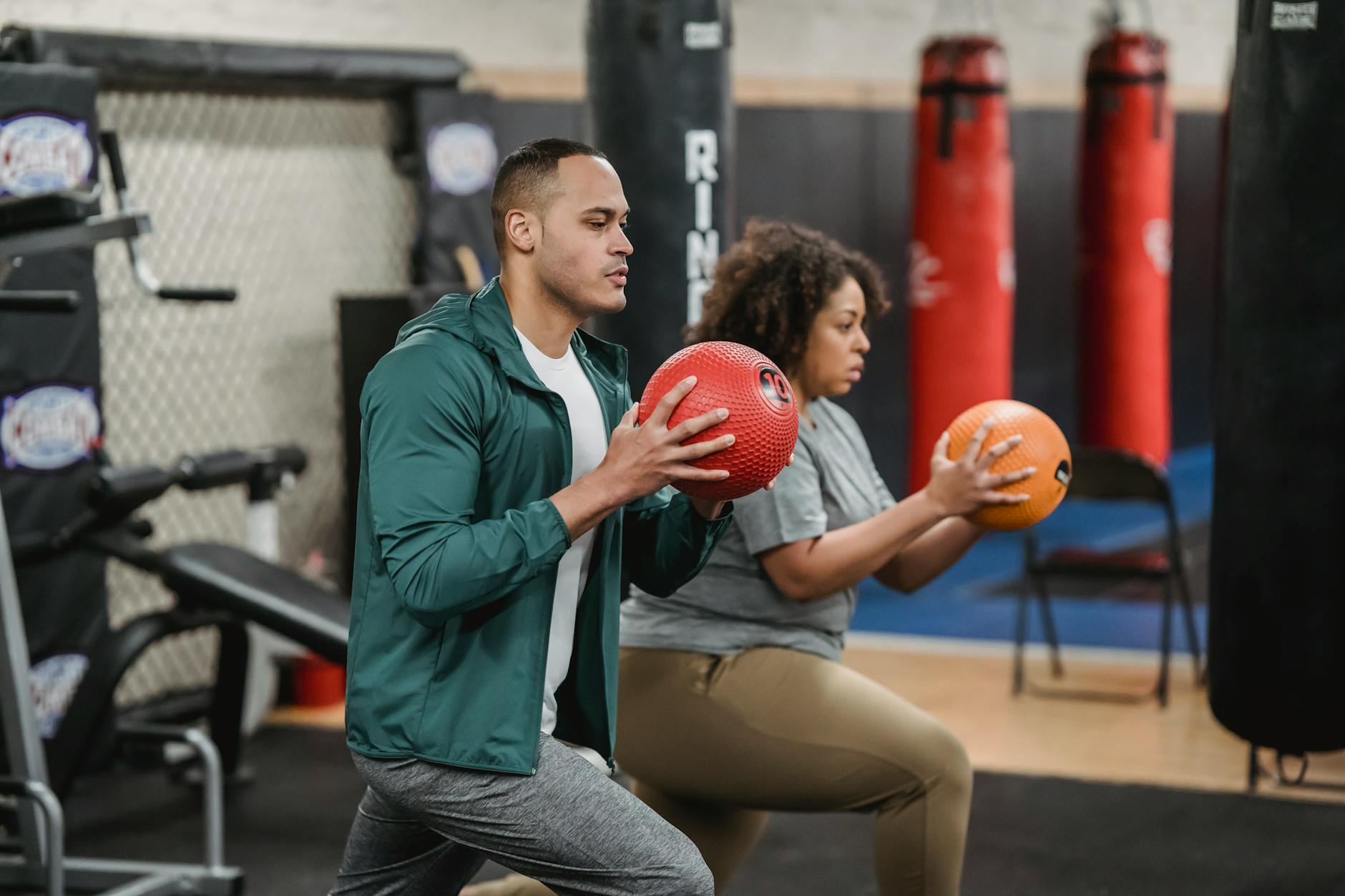 strong multiracial trainer and sportswoman doing lunges with balls in gym