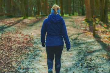 woman in blue hoodie walking on pathway to the woods