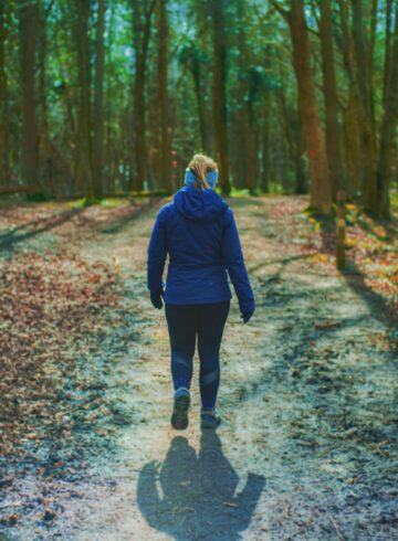 woman in blue hoodie walking on pathway to the woods
