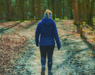 woman in blue hoodie walking on pathway to the woods